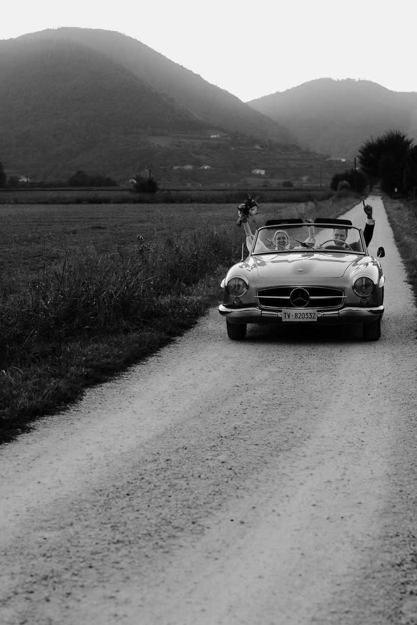 Un'auto d'epoca su una strada bianca tra le colline, in bianco e nero
